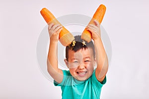 Child boy in turquoise shirt, holds huge carrots depicting horns - fruits and healthy food