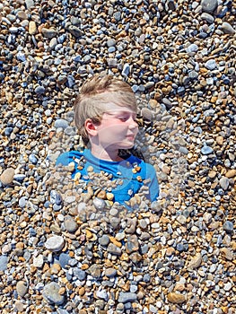 Child boy under pebbles stones on british seaside beach on sunny day