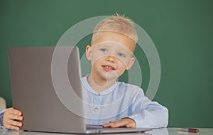 Child boy using a laptop computer at school. Cute pupil face closeup on blackboard background.