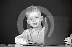 Child boy using a laptop computer at school. Cute pupil face closeup on blackboard background.