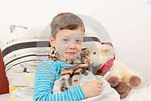 Child boy wrapped in a scarf in bed measures the temperature with a thermometer at a toy sheep