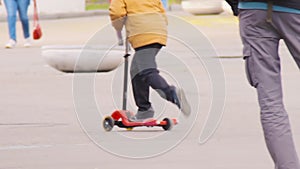 A child boy in a yellow jacket riding a scooter..