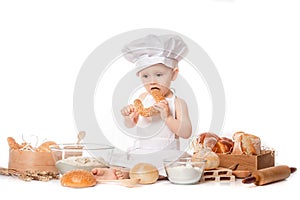 Child with bread on bakery-like background wearing cook-hat. Little baker baby boy