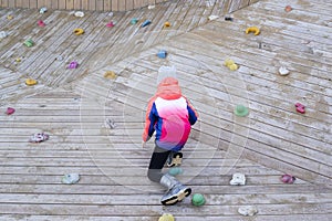 a child in a bright pink jacket is climbing a wooden wall photo