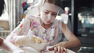 Child with a broken arm in a bandage draws with colored pencils. girl with plastered hand.