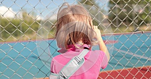 A child with a broken arm outdoors near a playground fence.