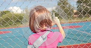 A child with a broken arm outdoors near a playground fence.