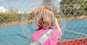 A child with a broken arm outdoors near a playground fence.