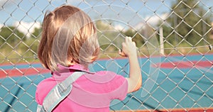 A child with a broken arm outdoors near a playground fence.