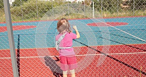 A child with a broken arm outdoors near a playground fence.