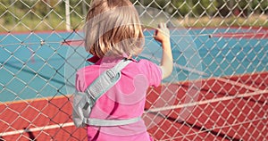 A child with a broken arm outdoors near a playground fence.