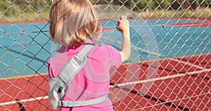 A child with a broken arm outdoors near a playground fence.