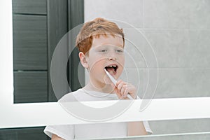 Child brushing teeth in front of mirror in bathroom in the morning