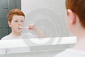 Child brushing teeth in front of mirror in bathroom in the morning