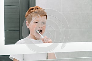 Child brushing teeth in front of mirror in bathroom in the morning