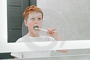 Child brushing teeth in front of mirror in bathroom in the morning. Personal hygiene