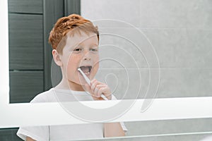 Child brushing teeth in front of mirror in bathroom in the morning. Personal hygiene