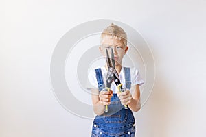 The child is the Builder holding a pair of tin snips in front of a white wall, space for text, concept of repair