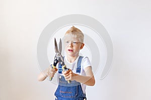 The child is the Builder holding a pair of tin snips in front of a white wall, space for text, concept of repair