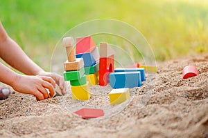 Child building house from wooden blocks in sandbox in summer