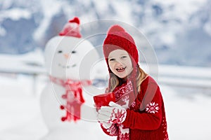 Child building snowman. Kids build snow man. Boy and girl playing outdoors on snowy winter day. Outdoor family fun on Christmas