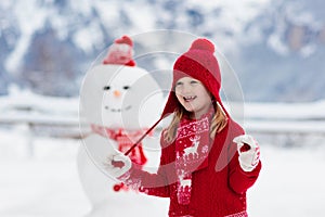 Child building snowman. Kids build snow man. Boy and girl playing outdoors on snowy winter day. Outdoor family fun on Christmas