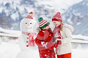 Child building snowman. Kids build snow man. Boy and girl playing outdoors on snowy winter day. Outdoor family fun on Christmas