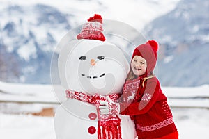 Child building snowman. Kids build snow man. Boy and girl playing outdoors on snowy winter day. Outdoor family fun on Christmas