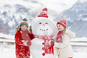 Child building snowman. Kids build snow man. Boy and girl playing outdoors on snowy winter day. Outdoor family fun on Christmas