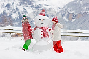 Child building snowman. Kids build snow man. Boy and girl playing outdoors on snowy winter day. Outdoor family fun on Christmas photo