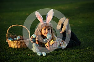 Child bunny boy with rabbit bunny ears. Easter egg hunt in garden. Child boy playing in field, hunting easter eggs.