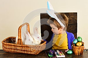 Child in bunny ears on Easter day. Cute boy with easters rabbit in basket and eggs.