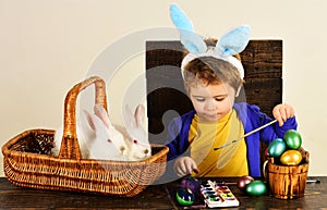 Child in bunny ears paint Easter egg. Little boy with easters rabbit in basket.