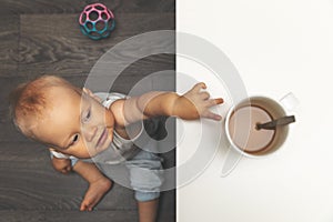 Child burn and scald injury concept - little boy reaching for hot drink mug on the table photo