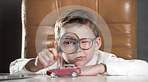 Child car expert. Kid with big magnifying glass observing a toy car. Businessman choose a car