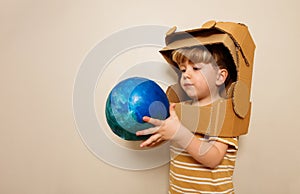 A child with cardboard astronaut helmet holds earth planet