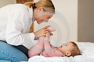 Child care. Happy woman making gymnastics to her baby girl, playing and bonding with infant, enjoying time together