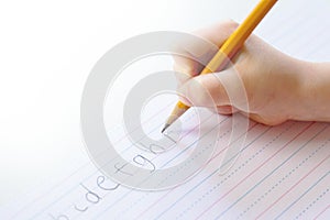 Child carefully prints alphabet on lined paper;