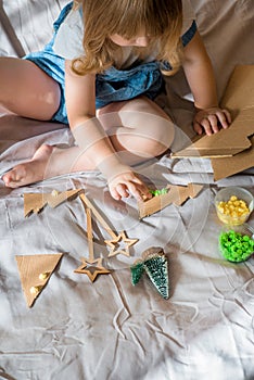 A child carves  Christmas tree from cardboard. Christmas decoration, hand made and Zero waste. child makes crafts on the bed at