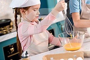 child in chef hat and apron whisking eggs