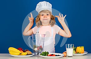 Child chef isolated on blue. Funny little kid chef cook wearing uniform cook cap and apron hold carrot cooked food in