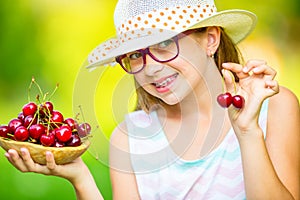 Child with cherries. Little girl with fresh cherries. Young cute caucasian blond girl wearing teeth braces and glasses.