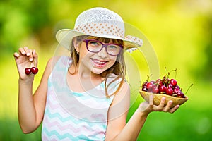 Child with cherries. Little girl with fresh cherries. Young cute caucasian blond girl wearing teeth braces and glasses.