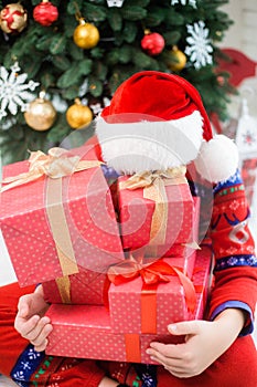 Child in christmas red hat hiding behind pile of holiday present