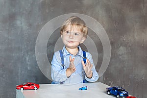 The child claps his hands. Portrait of a cute little boy playing with cars. Preschool boy playing with toy cars in kindergarten. E