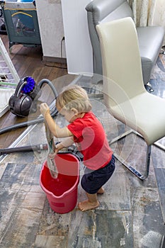 The child cleans the house, vacuums and wets a rag in a bucket of water to wash the floors.