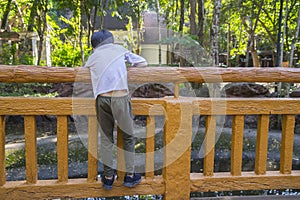 Child climbing a bridge fence by river or pond in a garden watching somthing