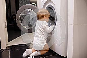 Child climbing into front-loading washing machine. Side view. Lack of parental supervision