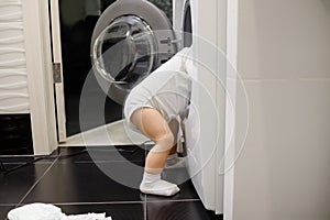 Child climbing into front-loading washing machine. Side view. Lack of parental supervision