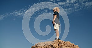 Child climbing the rock and looking forward with blue cloudy sky as background